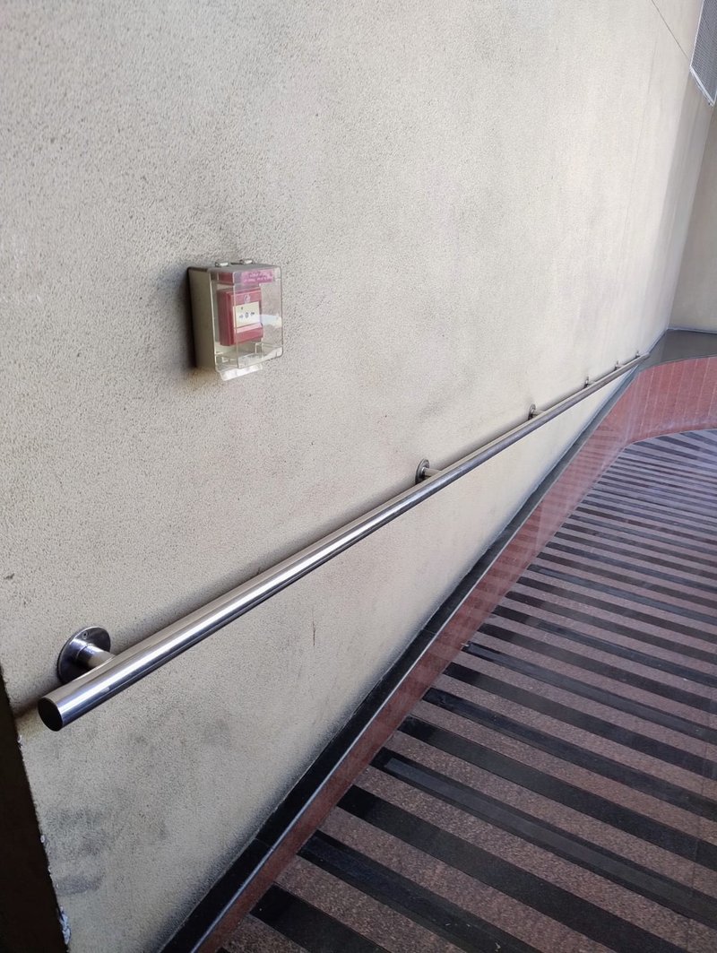 Wall-mounted tubular handrail along an access ramp